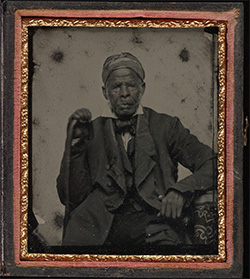 Said as an elderly man, seated wearing headwrap, suit; left elbow rests on newel, cane in right hand.